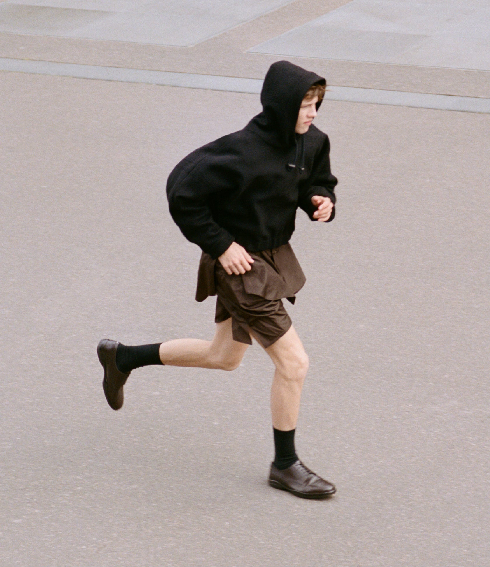 Person running on a paved surface wearing a black hoodie and brown shorts.